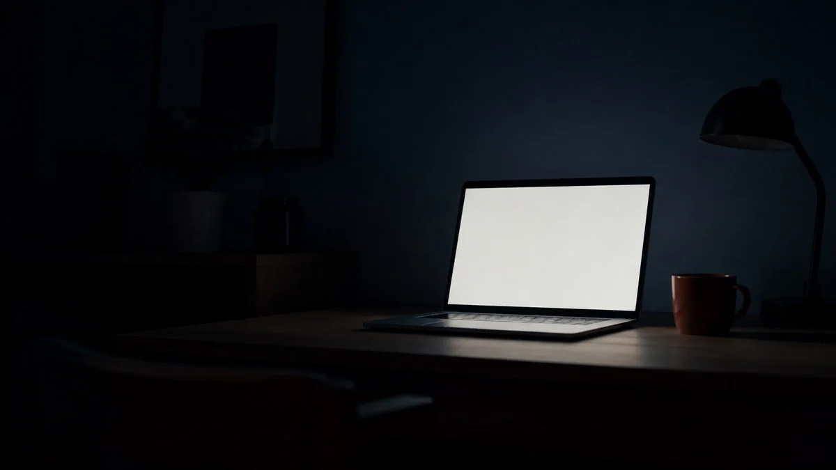 暗い部屋で、真っ白で何も表示されていない画面のノートパソコン
